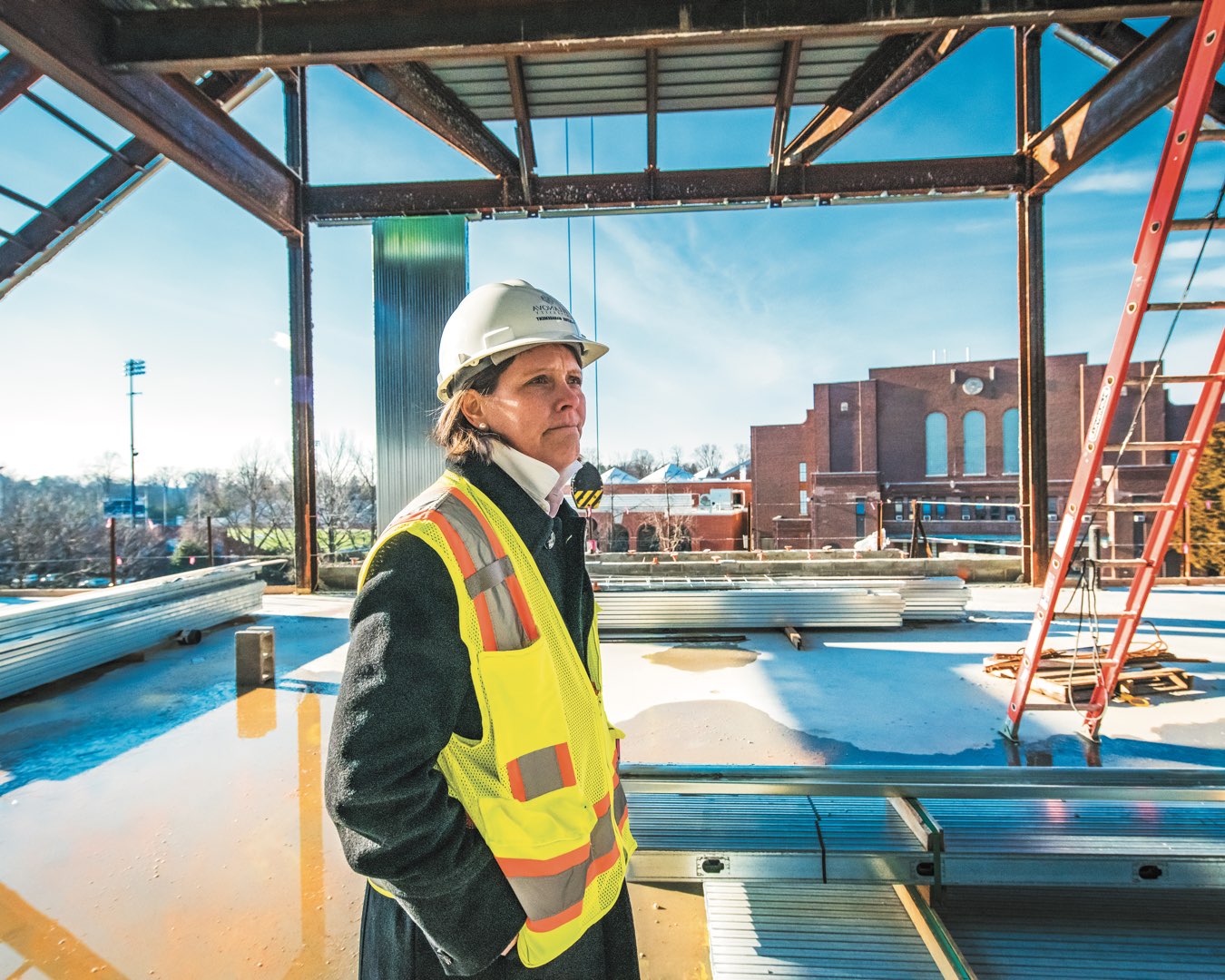 Marilou Smith in her bright yellow safety gear and hard hat looks out from the top of the future Performing Arts Center roof