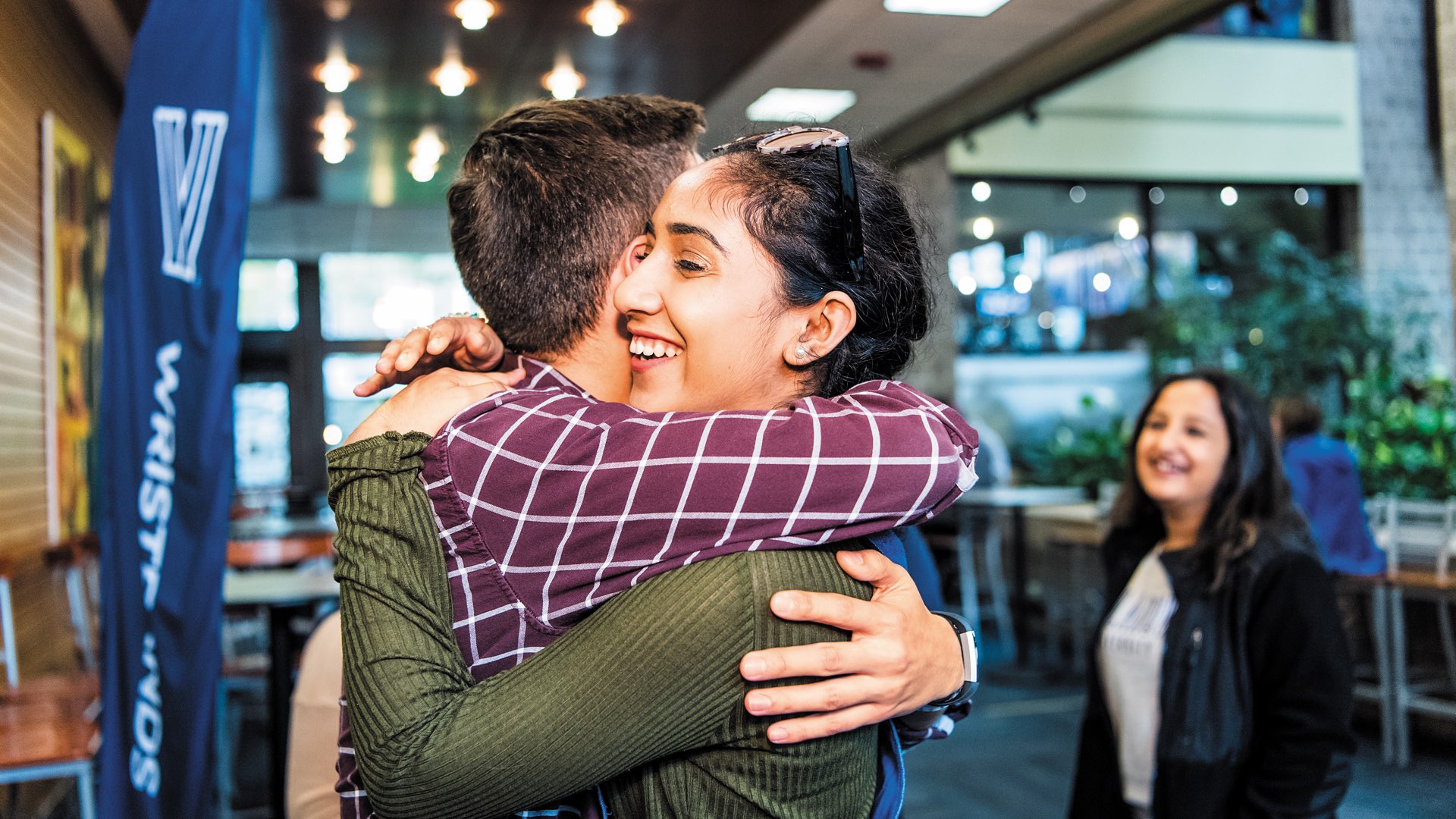 Young male and female alumni embrace at Villanova Reunion with another young alumna smiling in the background