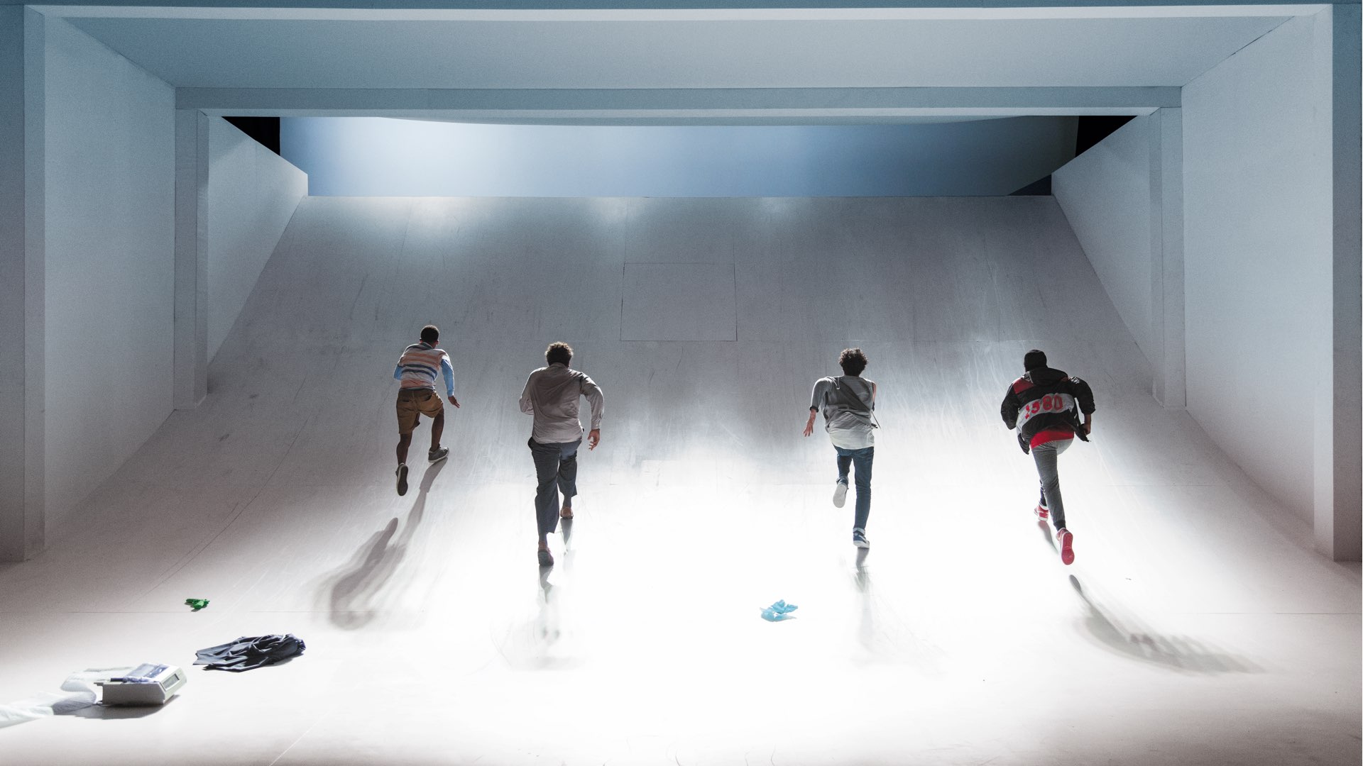 Young man in sweatpants and bright red Nikes laying with eyes closed in front of a printer printing a long list of names