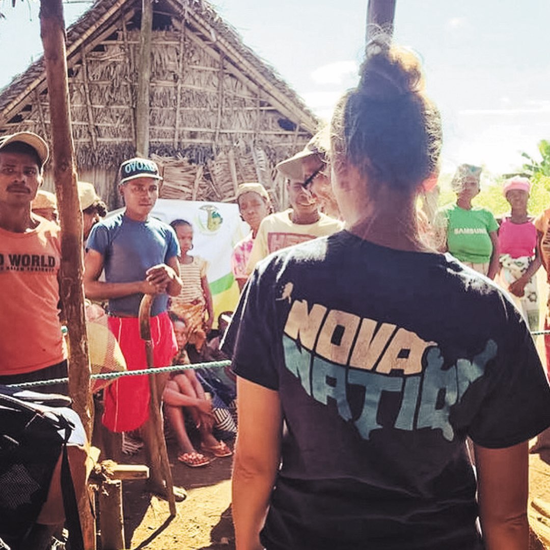 A female Villanova nursing student standing in front of a thatched hut talking with Malagasi villagers in Madagascar, Africa