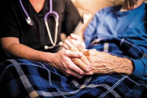 Health care worker’s hands holding an elderly person’s hands