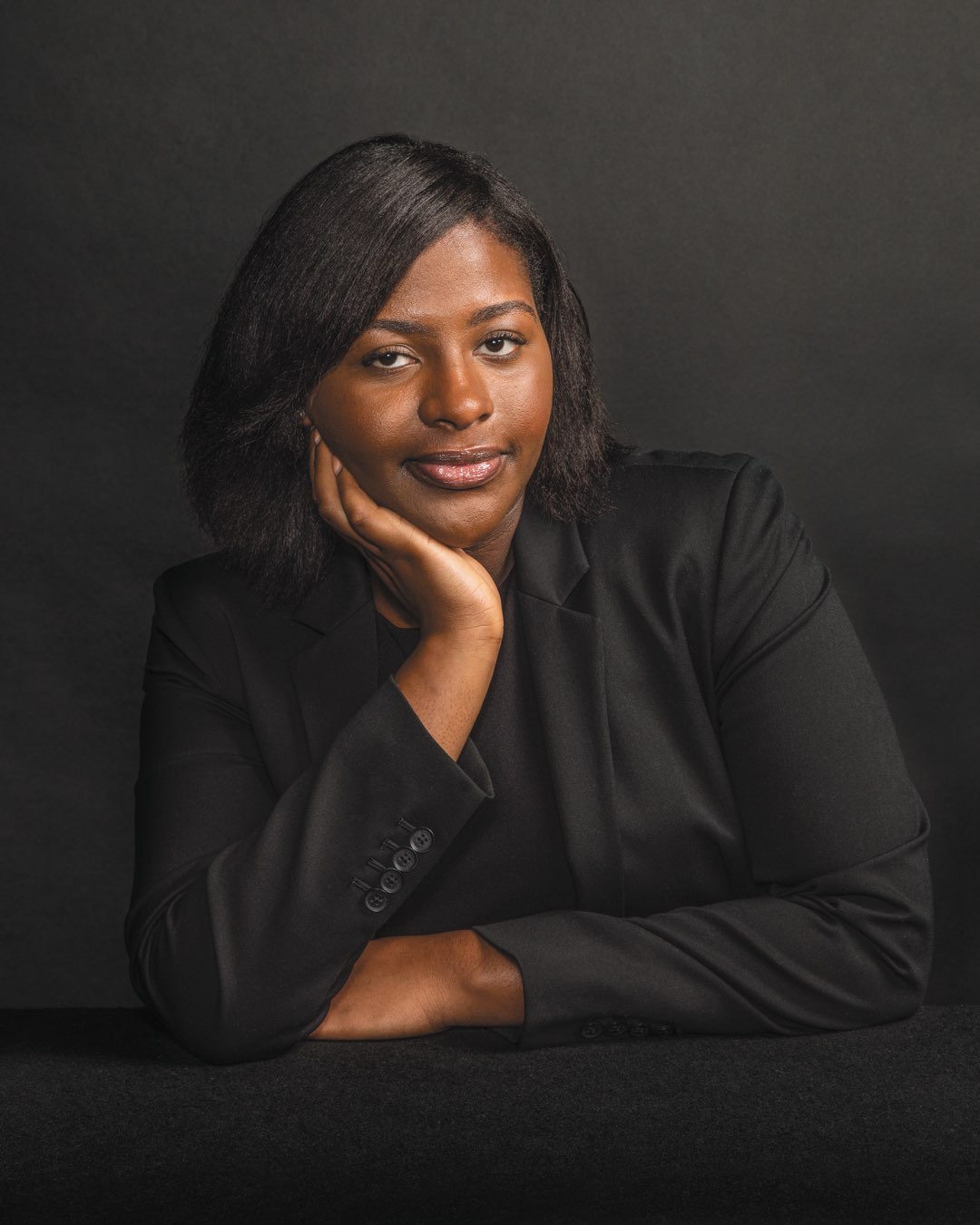 Recent graduate Mafatta Janeh leaning with arms folded and her hand on her chin in a black suit jacket