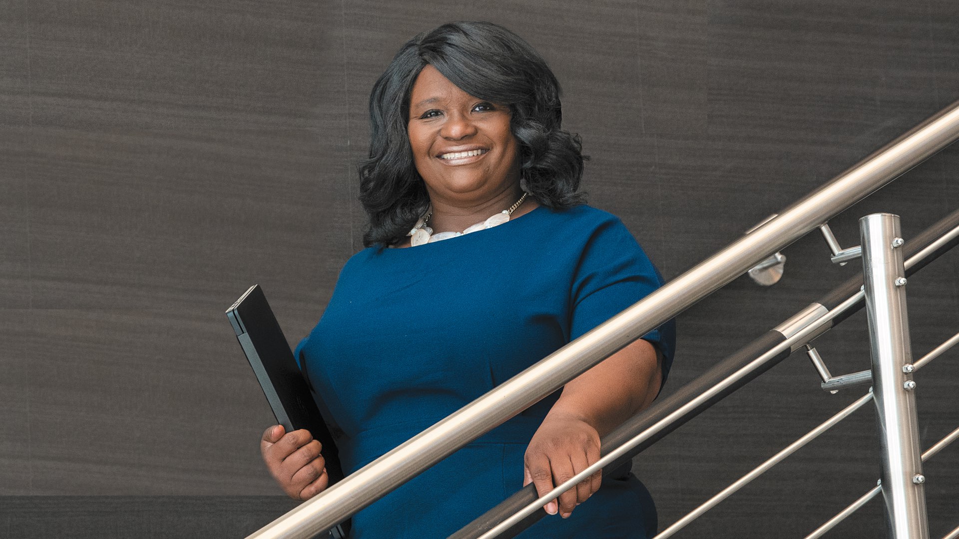 Wearing a navy career dress and holding a laptop, College of Professional Studies graduate Wanda Edmonson smiles