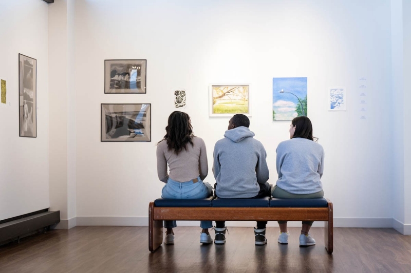 Three students sitting on a bench looking at artwork