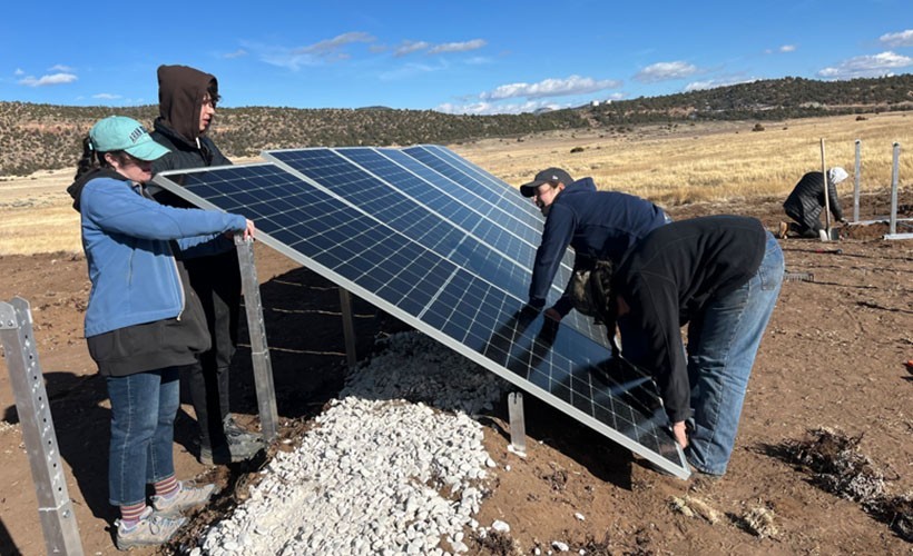 Four Engineering students adjust a solar panel in the desert.