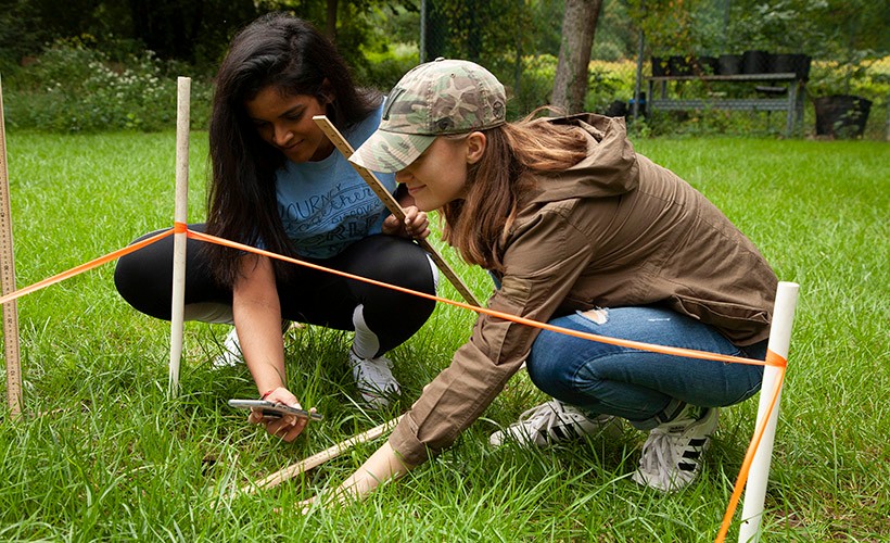 image of two female students measuring and taking pictures in a field.