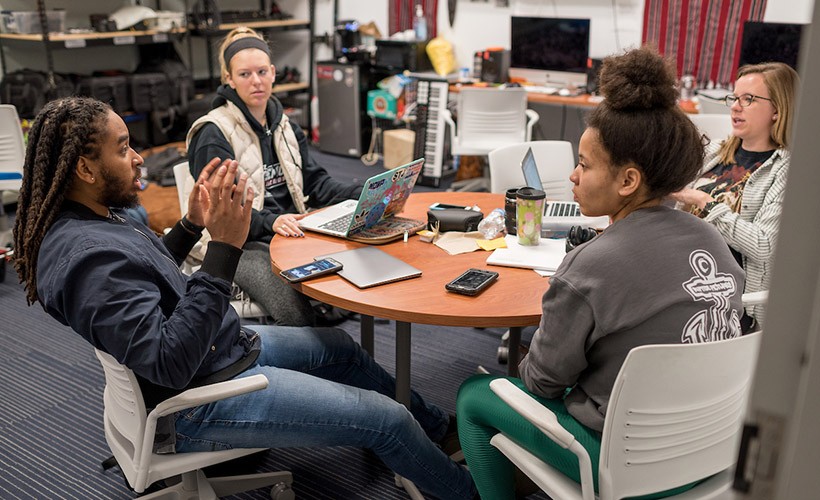 Student filmmakers sit in the editing room to discuss the project.