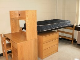 View of a desk and a bed with a three drawer dresser underneath in a Stanford Hall double room.