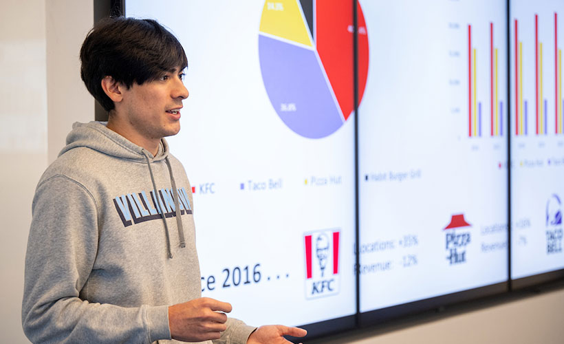 Male student speaking to class with presentation in background